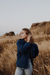 Young woman standing on field against sky