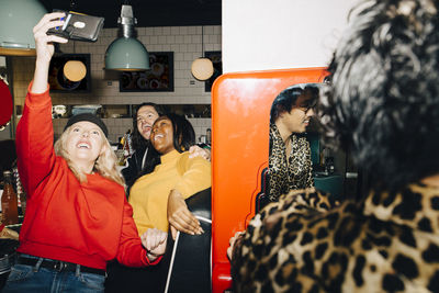 Smiling female taking selfie with friends in cafe