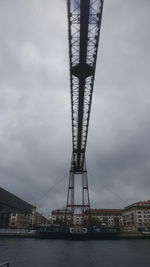 Suspension bridge over river against cloudy sky