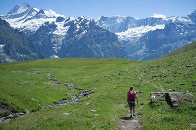 Rear view of woman walking on hills against snowcapped mountains