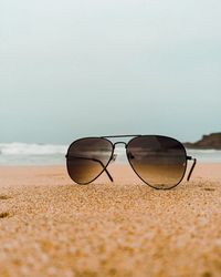 Close-up of sunglasses on sand at beach against sky