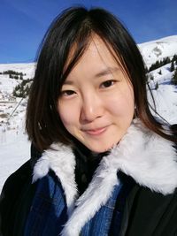 Close-up portrait of smiling young woman standing on mountain during winter