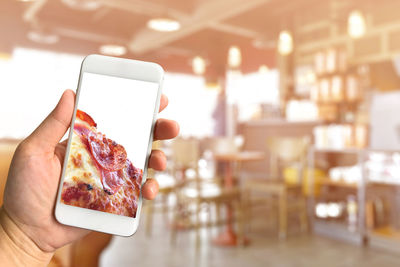 Cropped hands holding mobile phone with food picture on screen at cafe