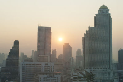 Modern buildings in city against sky during sunset