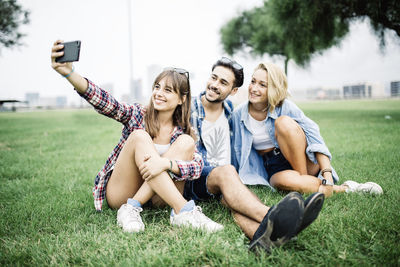 Full length portrait of young woman using phone while sitting on grass