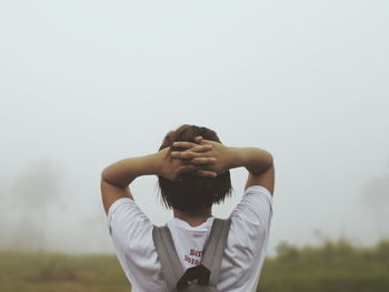 Rear view of woman with hands behind head against sky during foggy weather