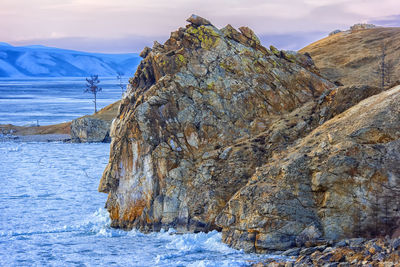 Snow covered rocks by sea against sky