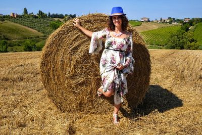 Portrait of smiling mid adult woman standing by hay bale on field