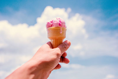 Hand holding ice cream cone against pink background