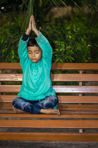 Young kid meditating at wood bench in traditional dress at evening from different angles