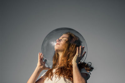 Low angle view of young woman wearing glass helmet in head against gray background