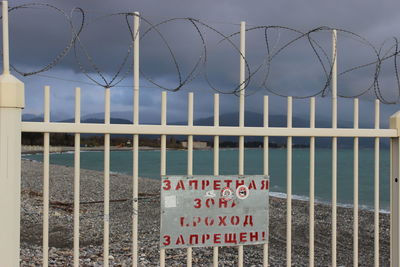 Information sign by fence against sky