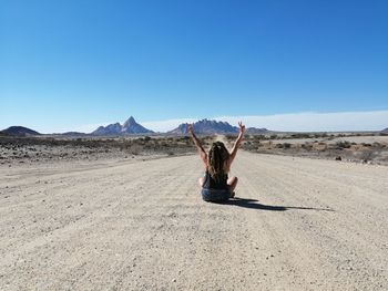 Woman with arms raised siting on road against sky