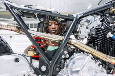 African american female mechanic with wrench fixing custom motorbike while working in workshop