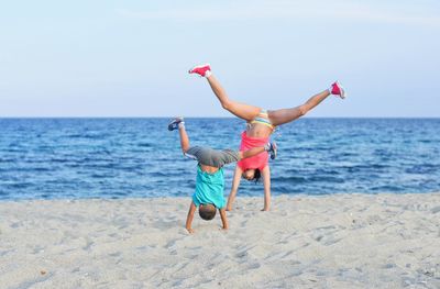 Children doing handstand on sand at beach against sky