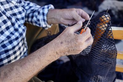 Midsection of man working on fishing net