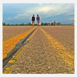 People walking on landscape against cloudy sky