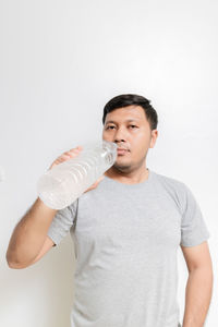 Young man drinking glass against white background