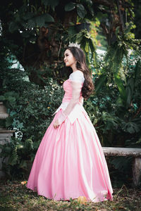 Full length of woman wearing crown looking away while standing against tree