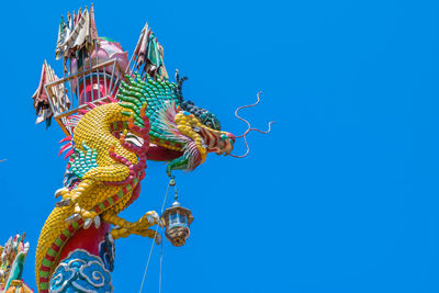 Low angle view of dragon statue against clear blue sky
