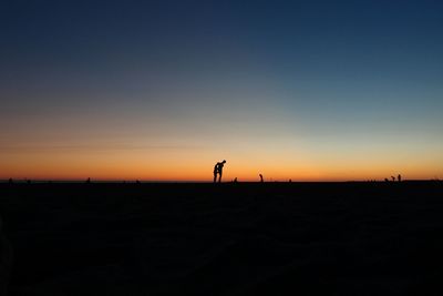 Silhouette man walking on sand at beach against clear sky