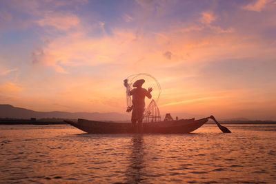 Silhouette fisherman fishing in sea against cloudy sky during sunset