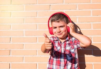 Cheerful boy listening music while standing against wall