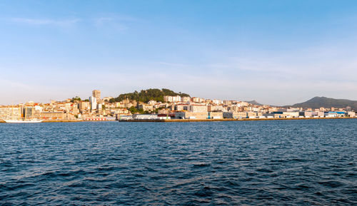 Buildings by sea against blue sky