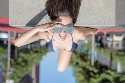 Portrait of young woman wearing sunglasses and bikini while lying on road in city during sunny day