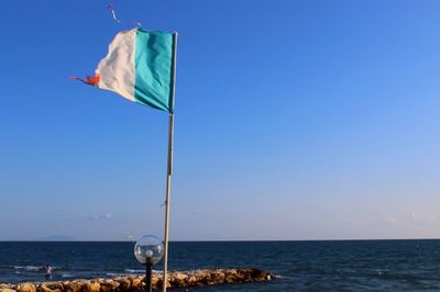 Flag on beach against clear blue sky