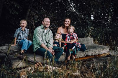 Happy family sitting on stone seat against trees