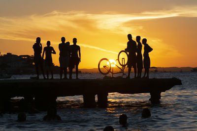Silhouette people on beach against sky during sunset