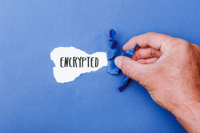 Cropped hand of person holding paper against blue background