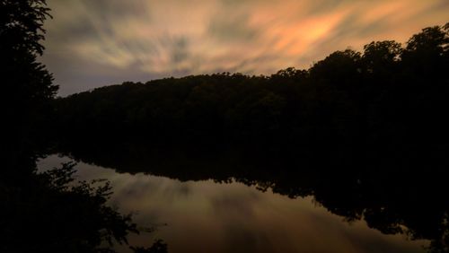 Silhouette trees by lake against sky during sunset