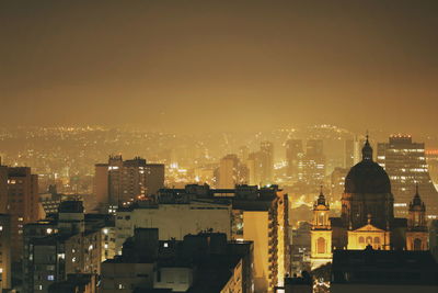 Illuminated buildings in city against sky during sunset