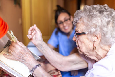 Happy senior woman with her caregiver at home reading a book. senior home care concept.