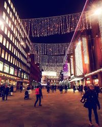 People on illuminated street amidst buildings at night