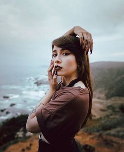 Portrait of young woman standing on cliff against sky