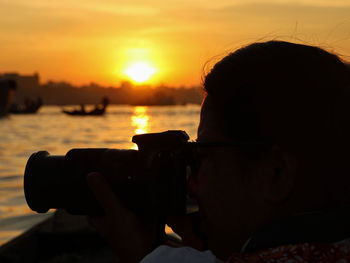 Portrait of man photographing against sky during sunset