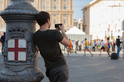 Rear view of man photographing athletes running during marathon in city