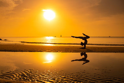 Silhouette person jumping on beach against sky during sunset