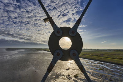 Metallic structure on land by sea against sky