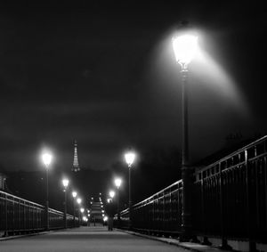 Illuminated street lights on bridge against sky at night