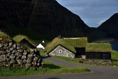 Houses by road against buildings and mountains against sky