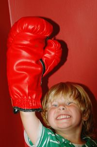 Portrait of cheerful boy wearing boxing glove against wall at home