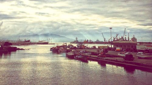 Boats in harbor against cloudy sky