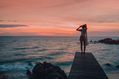 Man standing on rock against sea during sunset