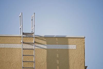 A yellow building and white fire escape ladder against a clear blue sky.