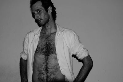 Portrait of man with fully unbuttoned shirt against wall