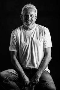 Portrait of smiling man sitting against black background